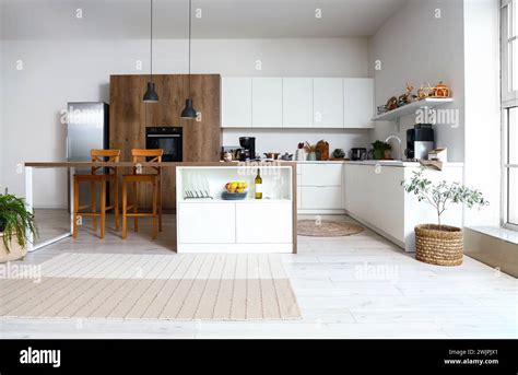 Interior of modern kitchen with white furniture and wooden island table ...