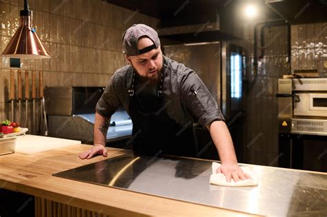 Premium Photo | Young male chef in uniform wiping stove surface with ...