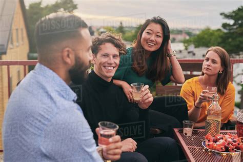 Cheerful friends enjoying social gathering on terrace during sunset ...